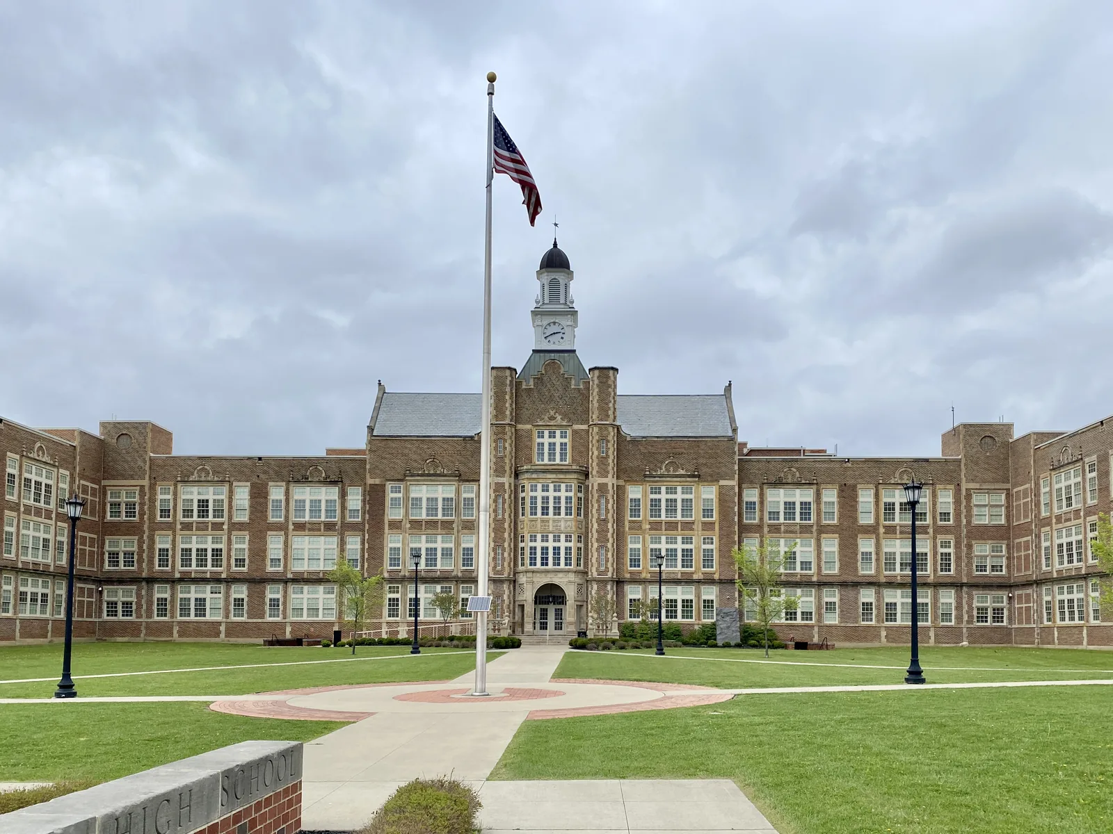 Built in 1926, this Jacobethan Revival-style building was likely designed by Walker and Weeks, and has served as a high school since its construction. The building was expanded with additions to accommodate increased student enrollment in the mid-20th Century, which eventually enclosed the front courtyard with a three-story Modern wing and extended the building to the rear. The building features a red brick exterior with sandstone trim, a tall central portion of the front facade with a clockto