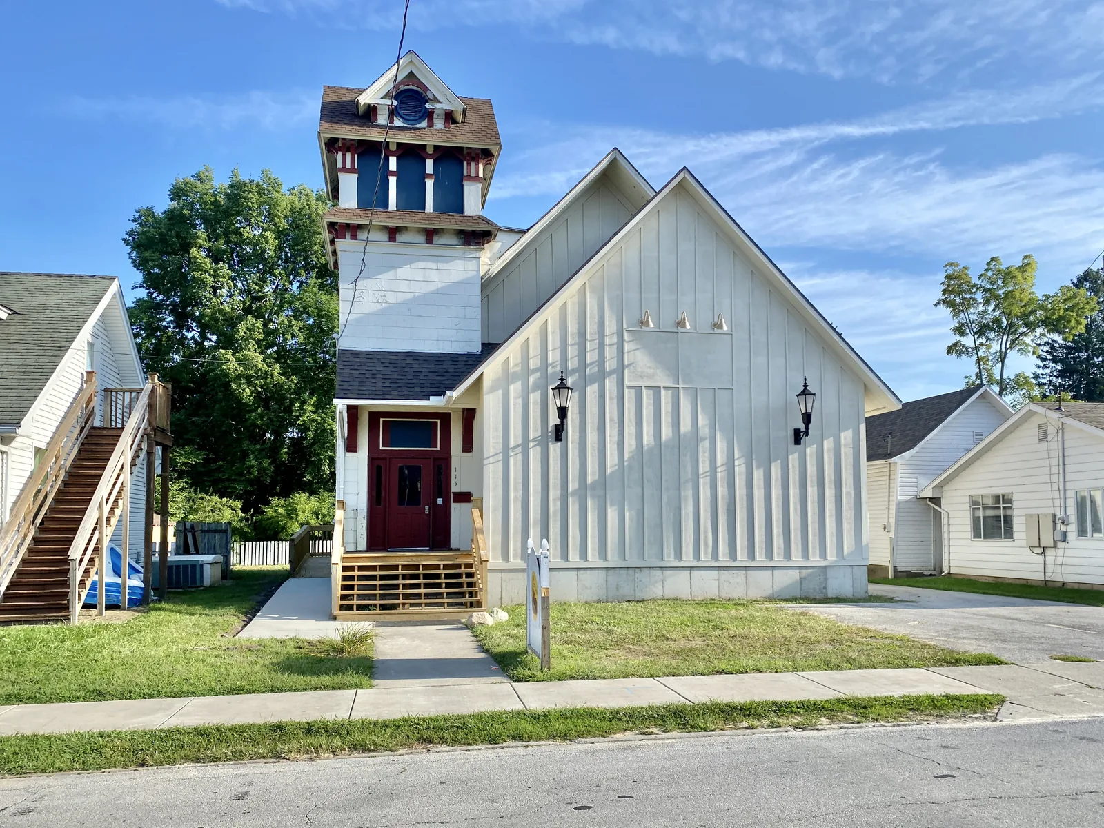 Former late 19th Century church, now home to a pre school, was recently stripped of its original front facade and diamond-pane windows in favor of blank front addition clad in board-and-batten “farmhouse”-style siding. The only remnant of the former Queen Anne and Carpenter Gothic-style structure is the tower, which is partially clad in asbestos shingle, but features bracketed eaves, a side gable roof, and decorative wooden trim.