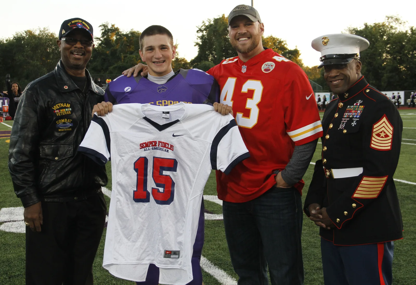 Jaycee Pummill, Blue Springs High School senior long snapper and a 2015 Semper Fidelis All-American Bowl selectee, is presented his jersey by Carson Ross, Blue Springs mayor, Thomas Gafford, Kansas City Chiefs long snapper, and Sgt. Maj. Johnnie Hughes, Marine Corps Recruiting Station Kansas City sergeant major, at Peve Stadium Oct. 3, 2014. Pummill is the only player selected from Kansas or Missouri to participate in next years bowl game. The Semper Fidelis Bowl is slated to be played Jan. 4, 2