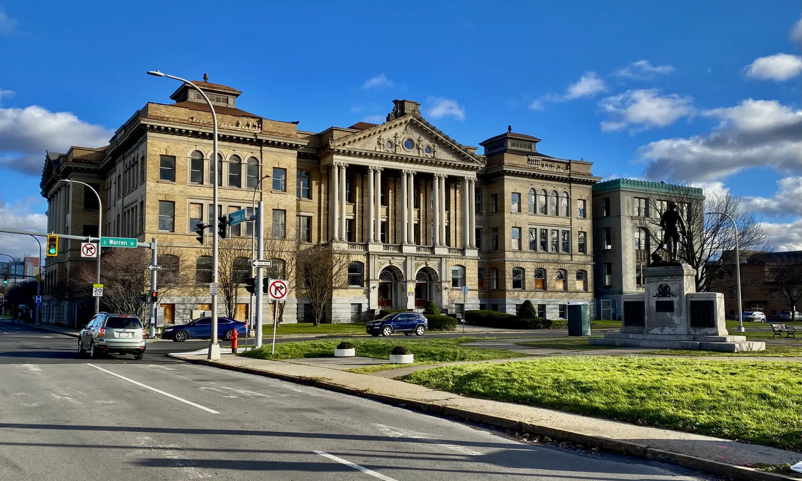 As seen in downtown Syracuse, New York in December 2021, the triangular Billings Park (bounded by South Salina, East Adams, and South Warren Streets) makes a pint-sized but pleasantly verdant foreground to the majestic former Central Technical High School, a 1903 masterwork by architect Archimedes Russell. An example of the Italian Renaissance Revival style with almost impossibly ornate Classical detailing, the central feature of this magnificent building is a double round-arched main entrance t